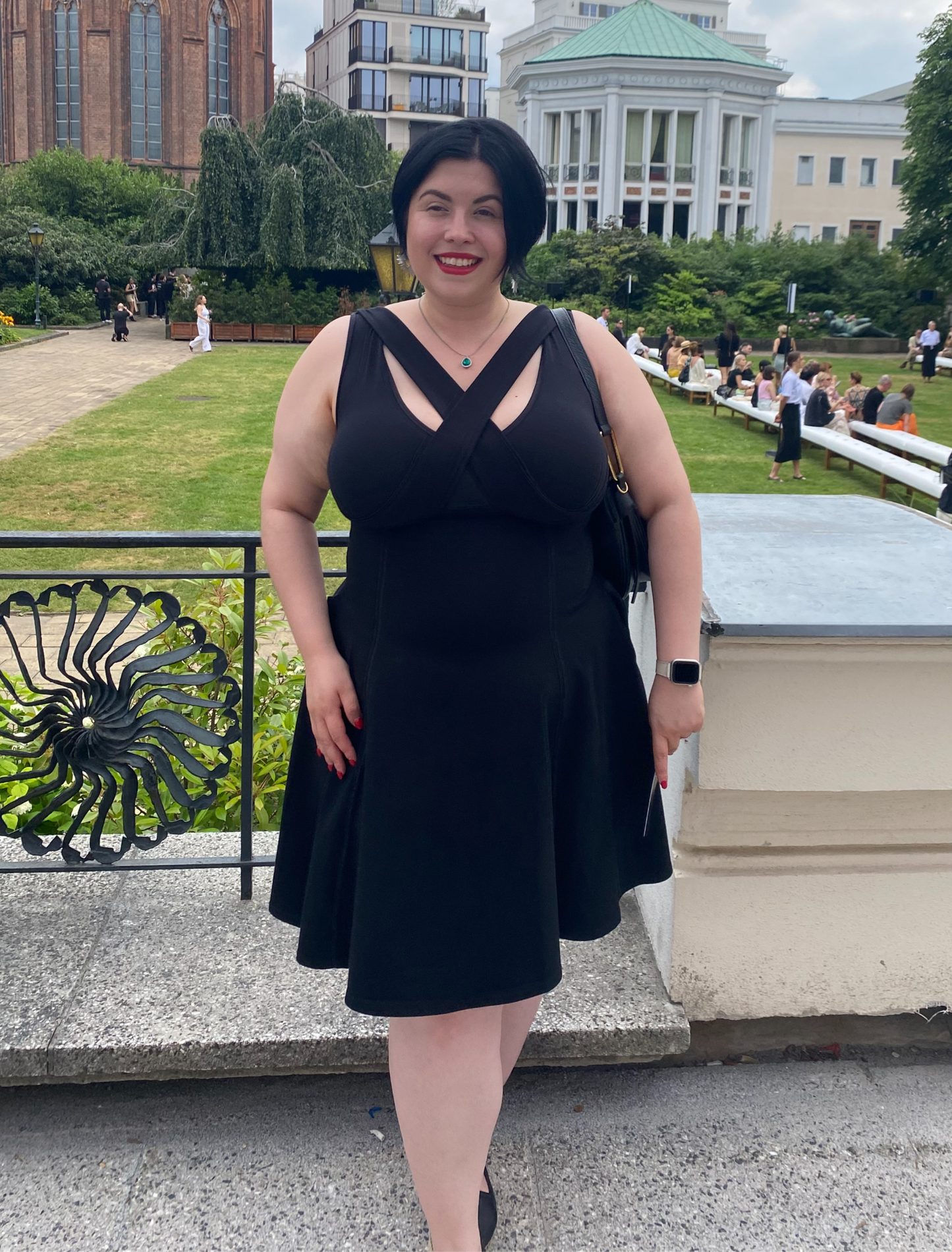 Woman standing outside in a city, right hand in pocket, wearing black flare dress.
