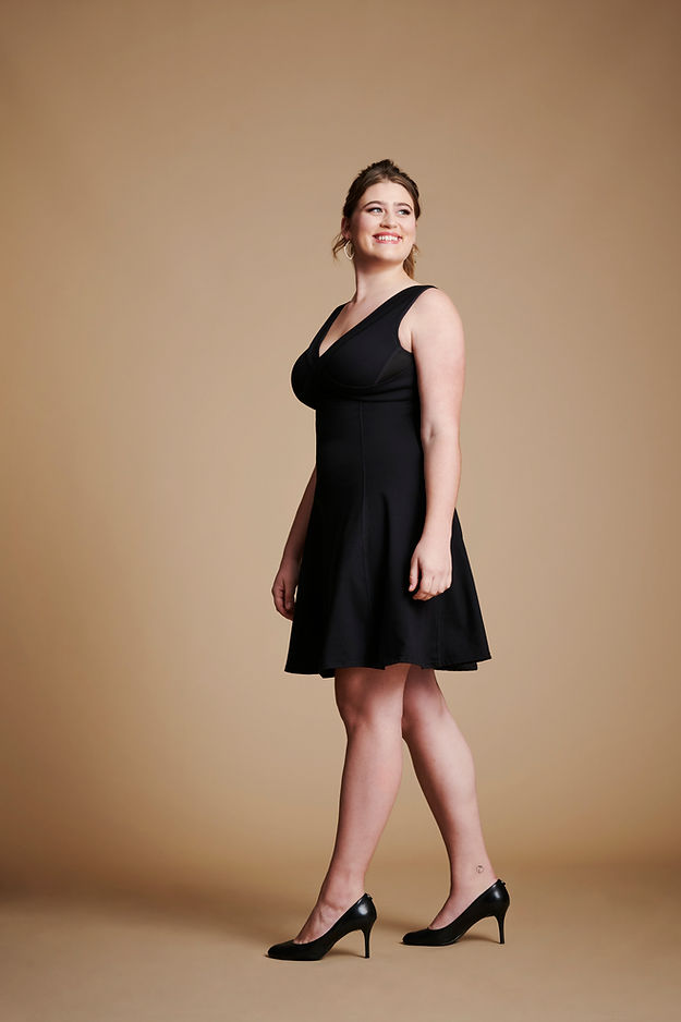 Front left view of woman wearing black flare dress with v neck.