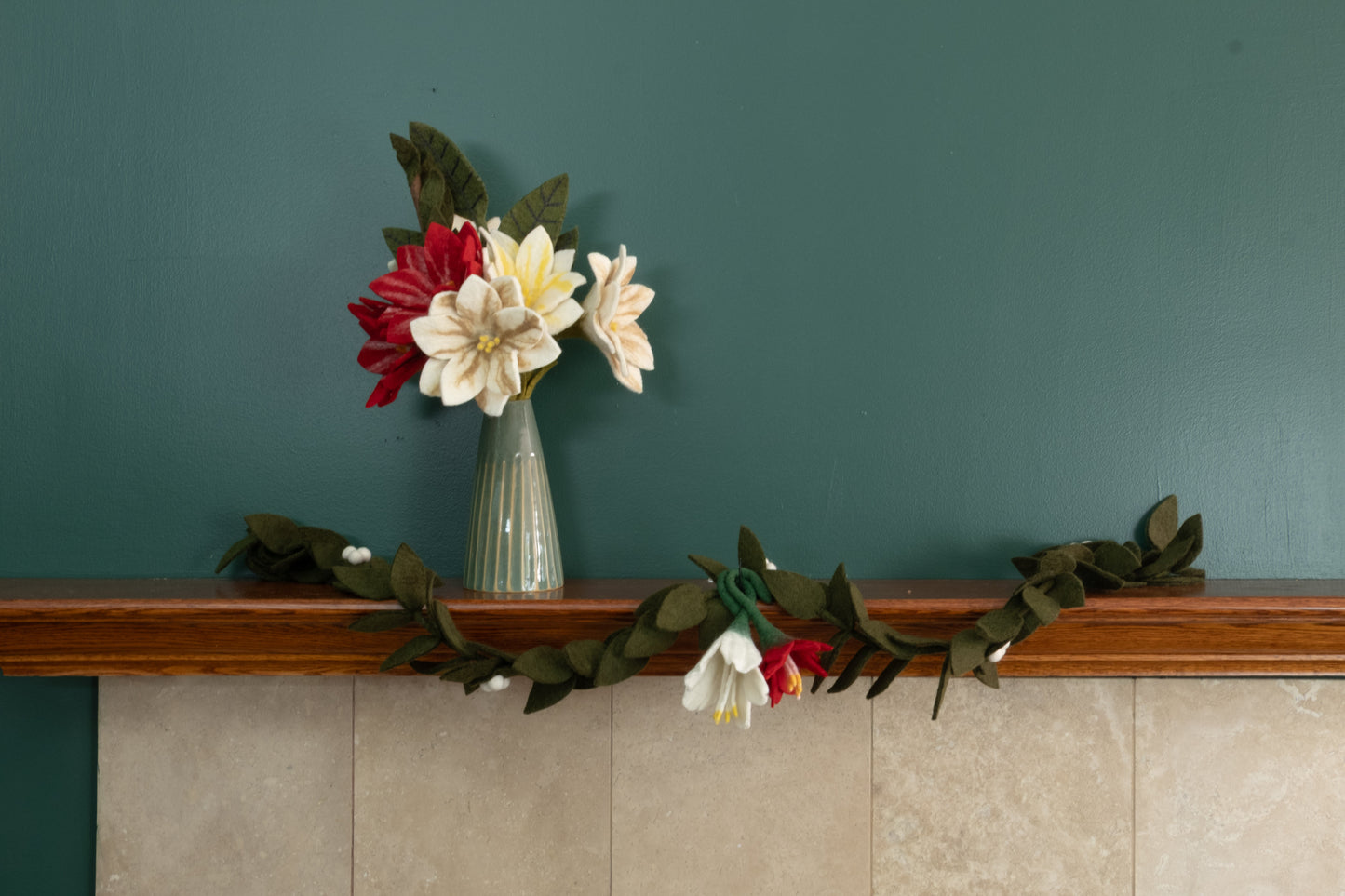 Felt ornaments of a red flower and a white flower hanging from a mantel decorated with Christmas flowers and garlands.