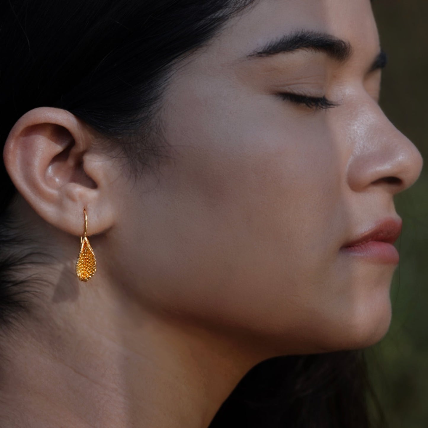 Front right view of woman wearing gold plated beeja Pod earrings.