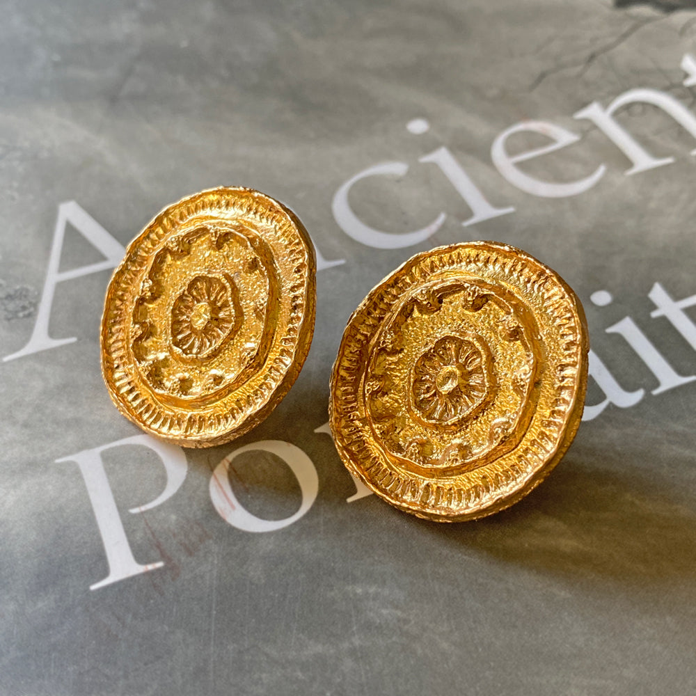 Pair of gold mandala earrings on grey background with letters.