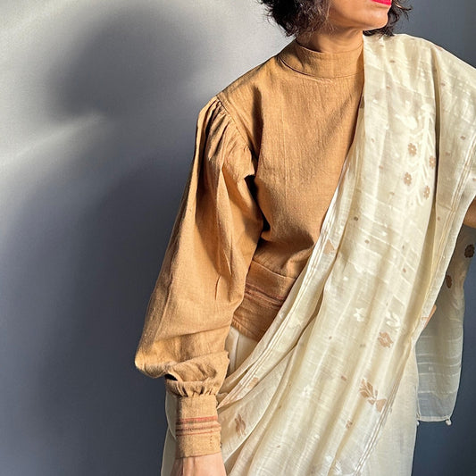 Partial view of woman wearing brown woven long sleeve shirt and cream colored wrap.
