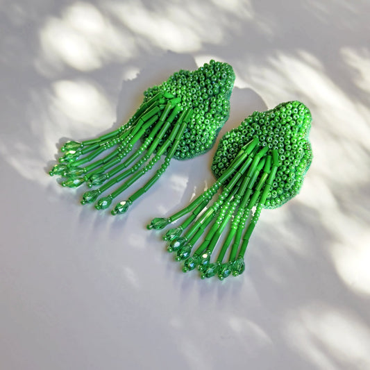 Pair of beaded green glass tassel earrings on shadowy background.