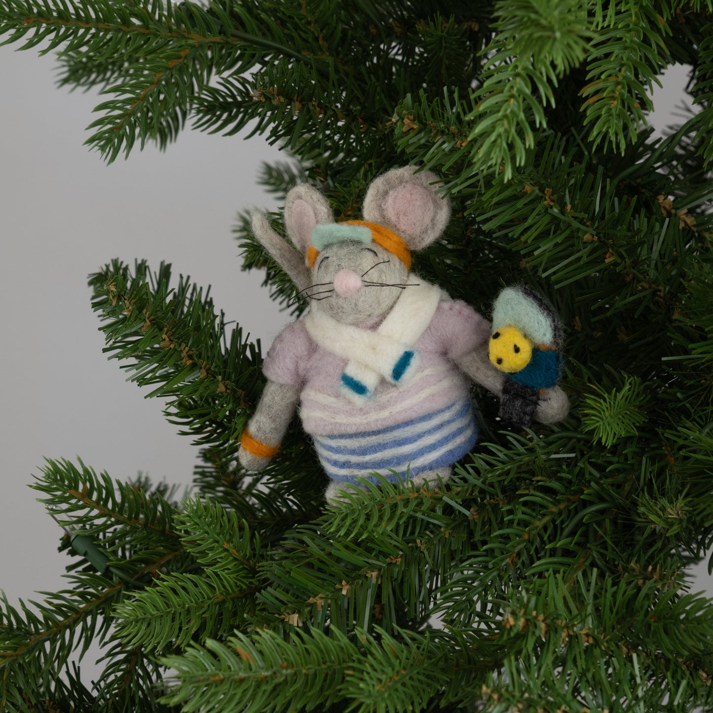 Felted ornament of a mouse dressed in a retro striped sweater, matching skirt, bright orange visor, and tiny sweatbands, with a pickleball paddle and ball in paw on a Christmas tree.