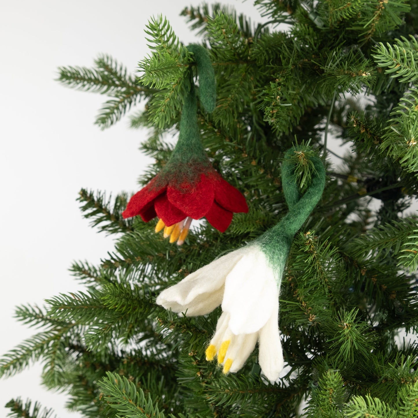 Felt ornaments of a red flower and a white flower on a Christmas tree.