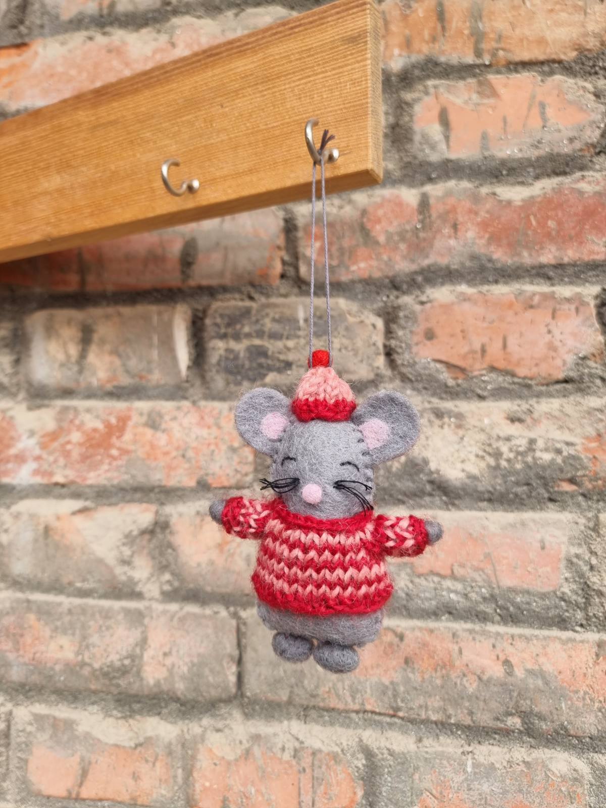 Felt ornament of a grey mouse in a red and white striped knitted sweater and hat hanging from mantel.