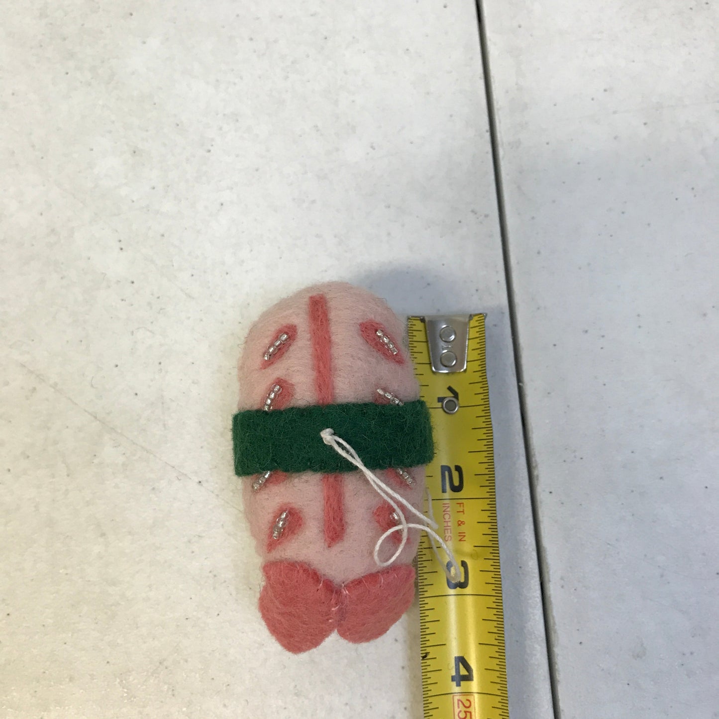 Felt ornament of shrimp sushi next to measuring tape showing it is 4 inches long.