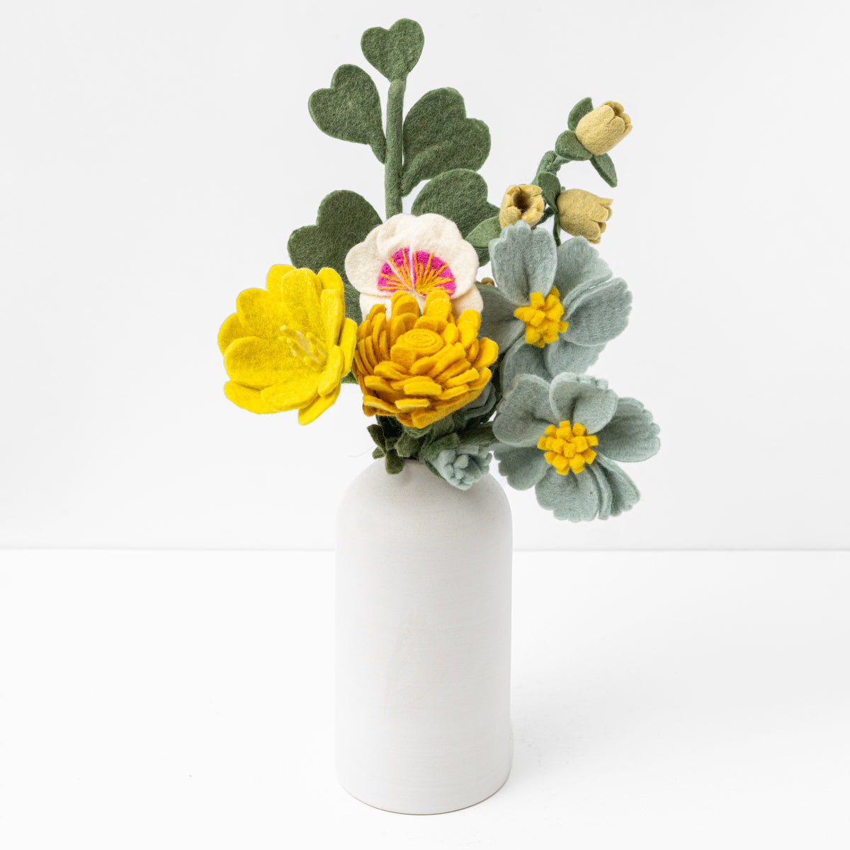 Felt flower bouquet of yellow, orange and white flowers with green leaves in a white vase with white background.