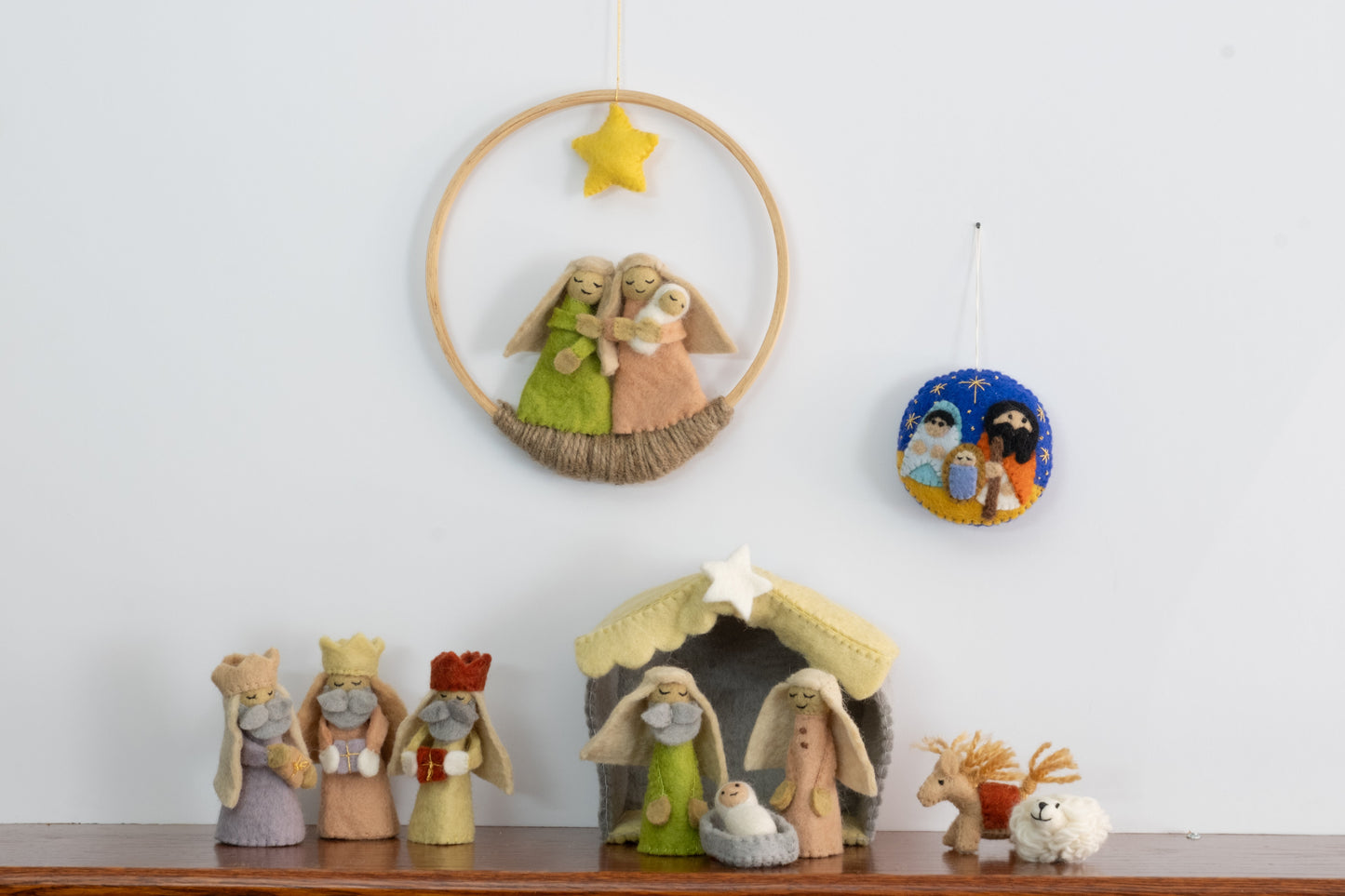 Felt ornament in a circle shape showing the nativity scene of Mary, Joseph, and baby Jesus underneath the night sky behind a full nativity scene set.