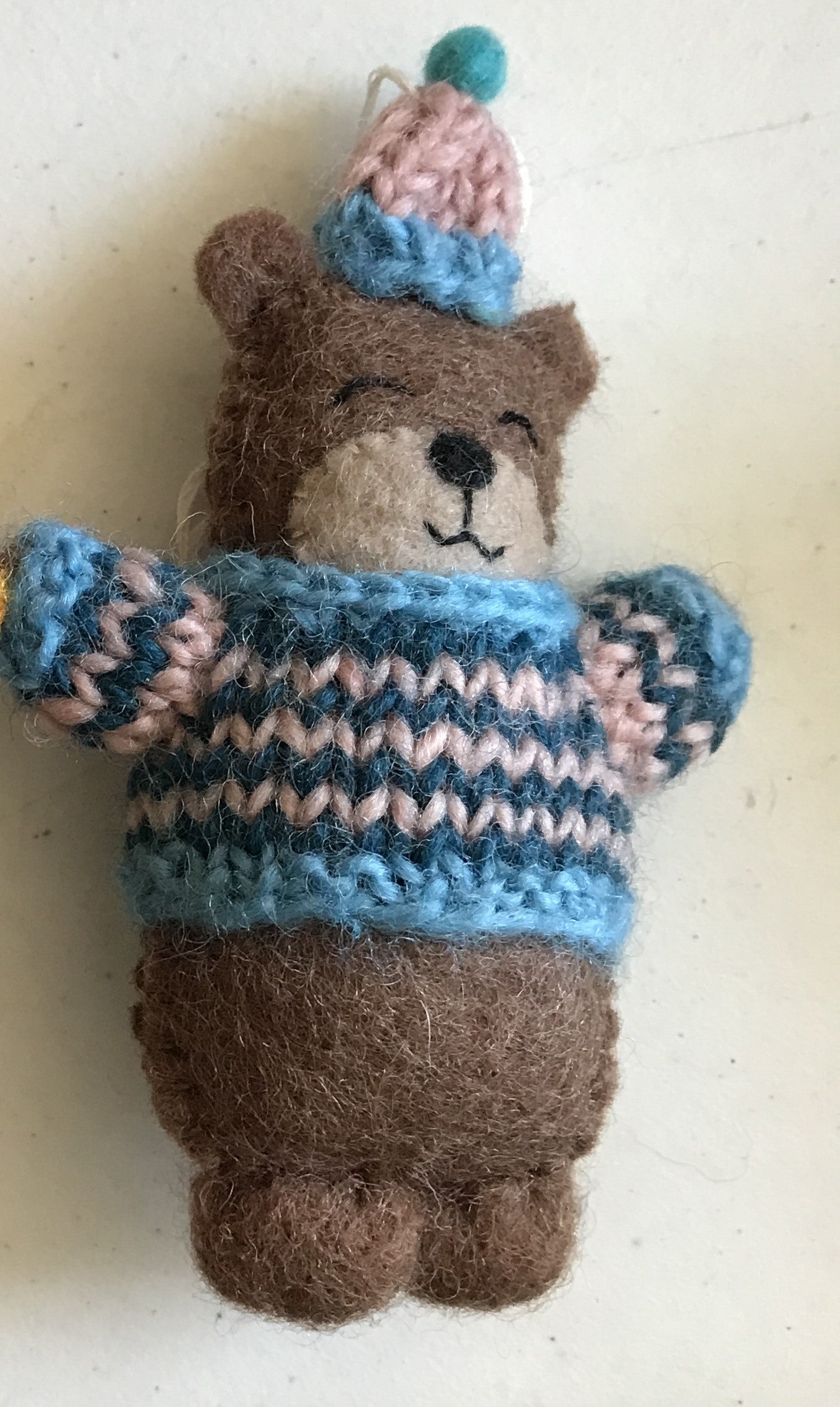 Close up of a felt ornament of a bear in a blue and pink striped knitted sweater and hat.