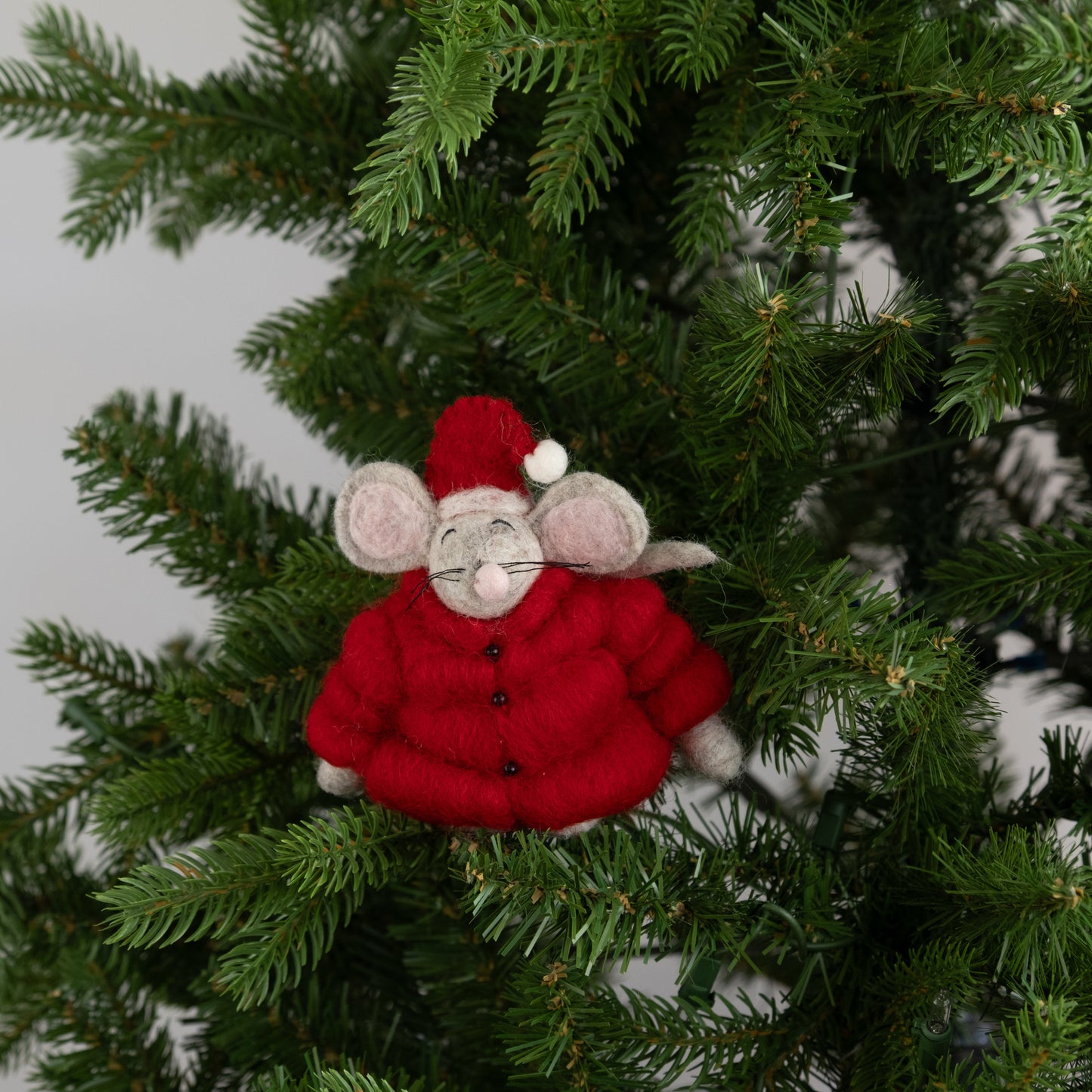 Felt ornament of a mouse in red puffer jacket and Santa hat on a Christmas tree.