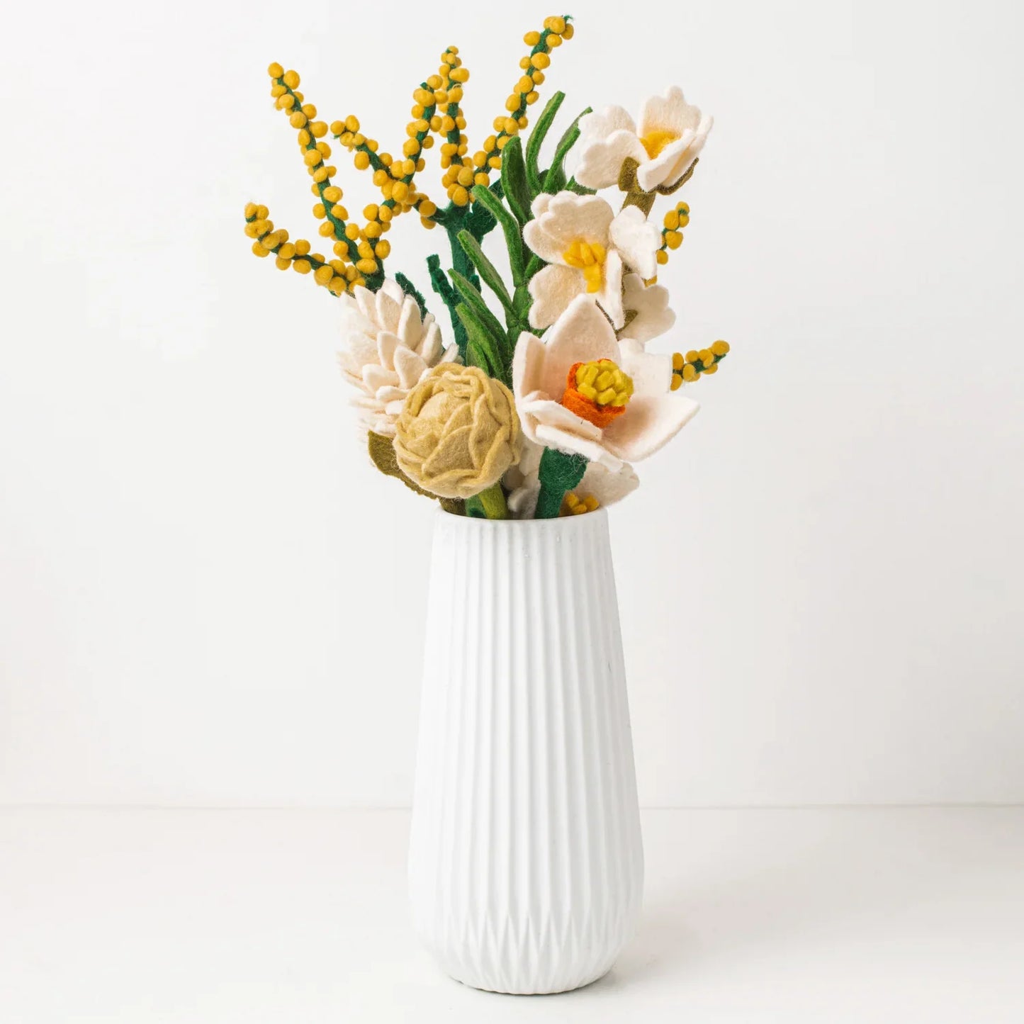 Yellow, white, orange, green felt floral arrangement in a white vase.