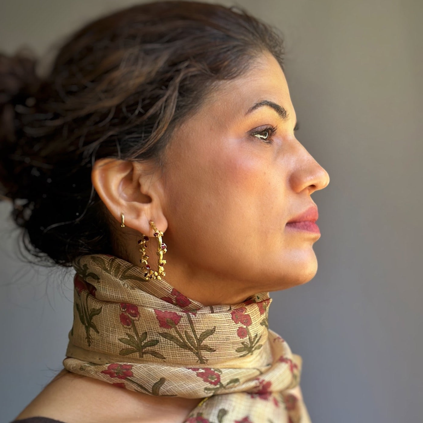 Right front view of woman wearing red and gold hoop earrings.
