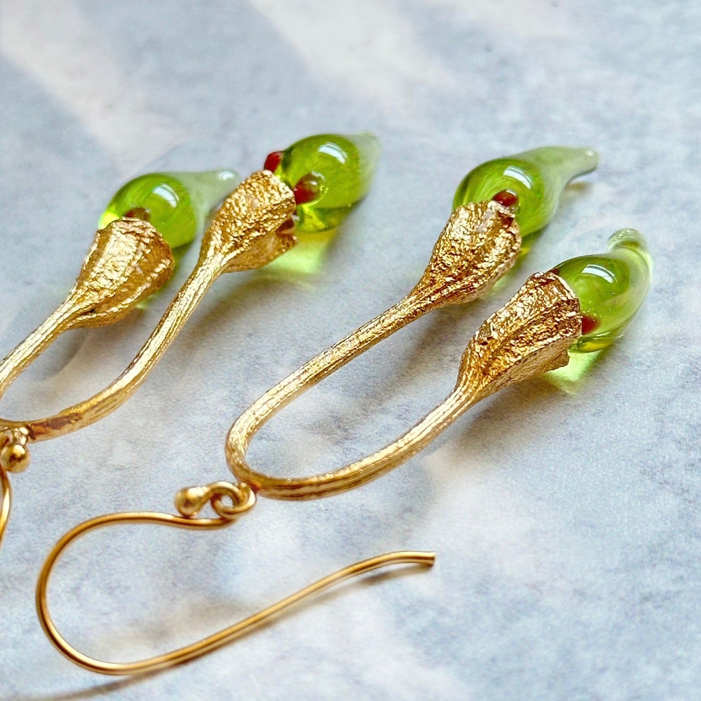 Pair of green and gold double chili pod earrings with silver colored findings.