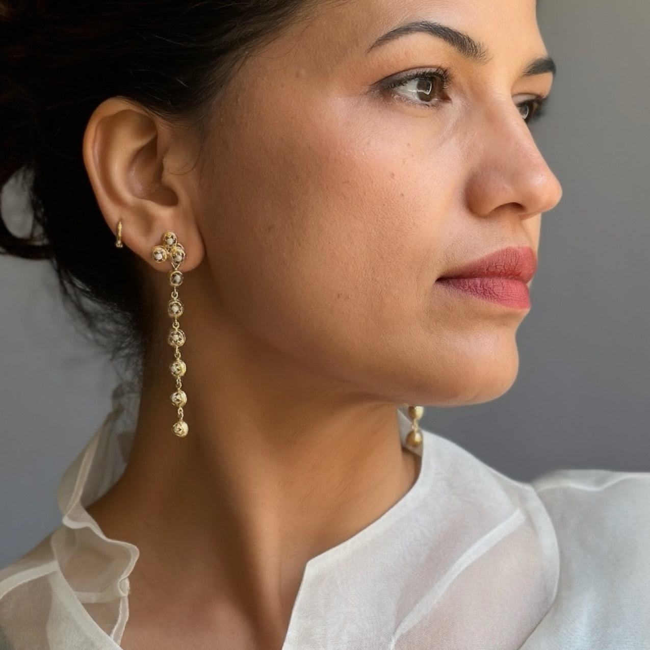 Front right view of woman wearing gold dangle earrings with five discs each and pearl glass in each disc.
