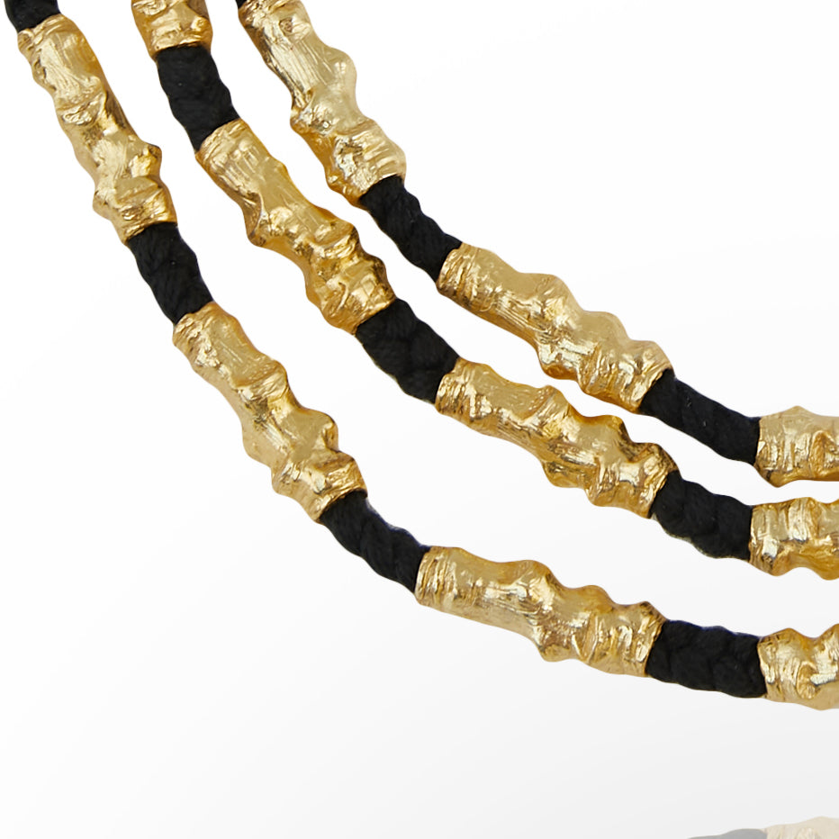 Closeup of three gold plated and black thread necklaces