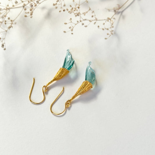 Pair of blue twisted glass petal earrings with gold findings upside down and dried flower twig above.