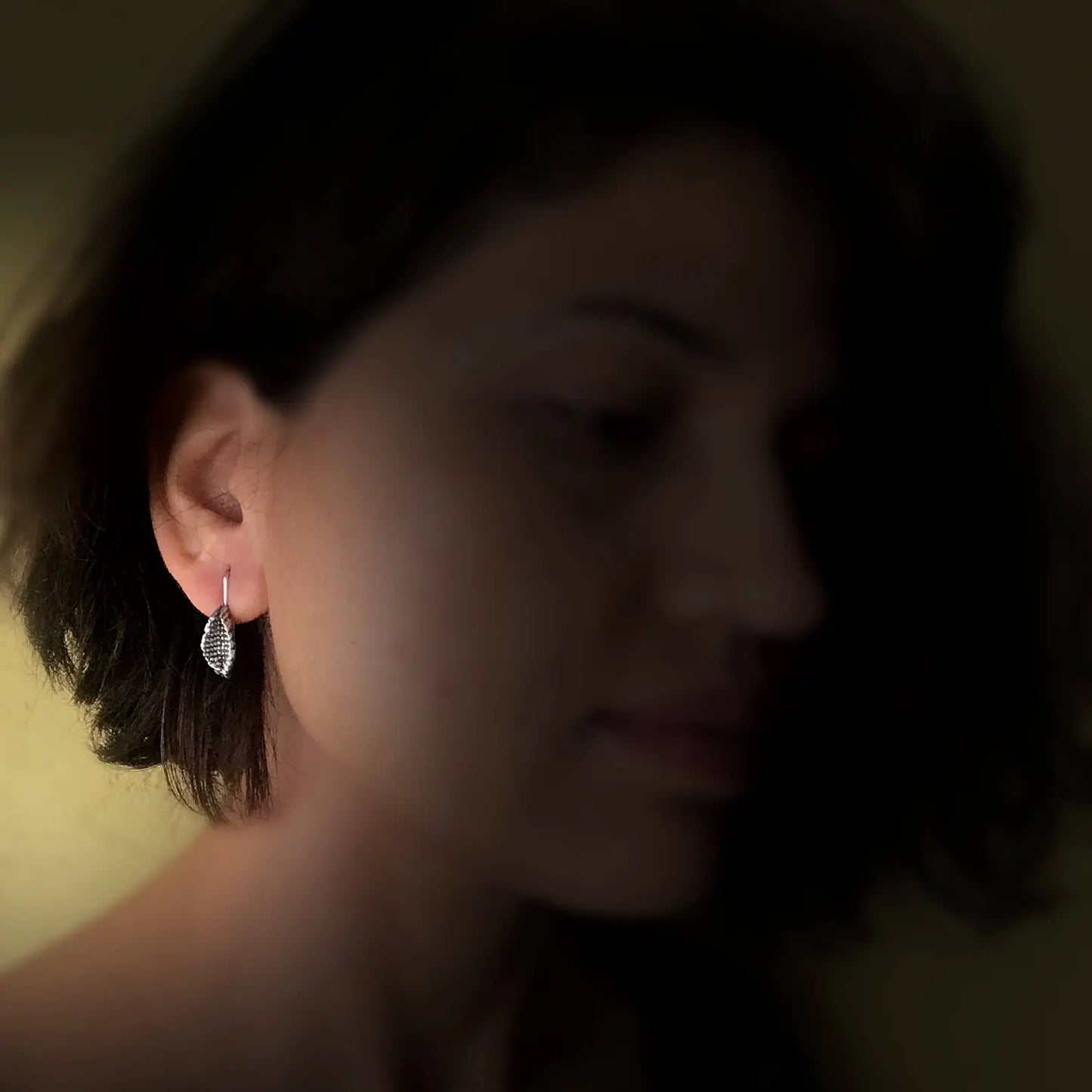 Front right view of woman in shadows wearing silver beeja Pod earrings