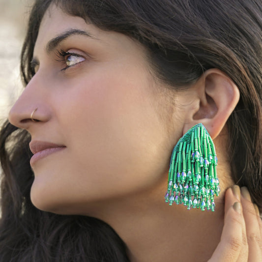 Front left view of woman wearing beaded green glass tassel earrings.