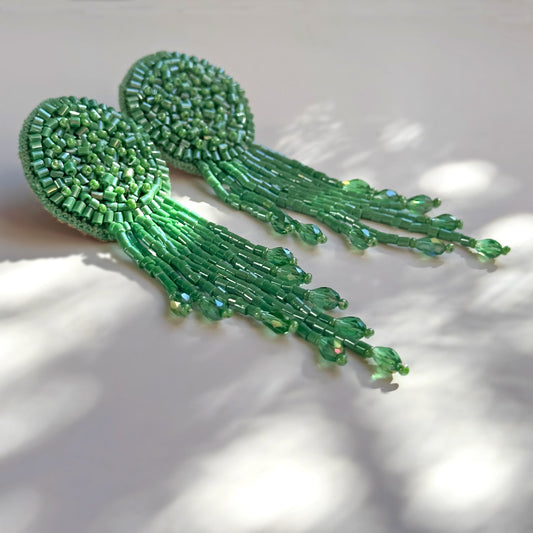 Pair of green glass beaded tassel earrings on shadowy background.