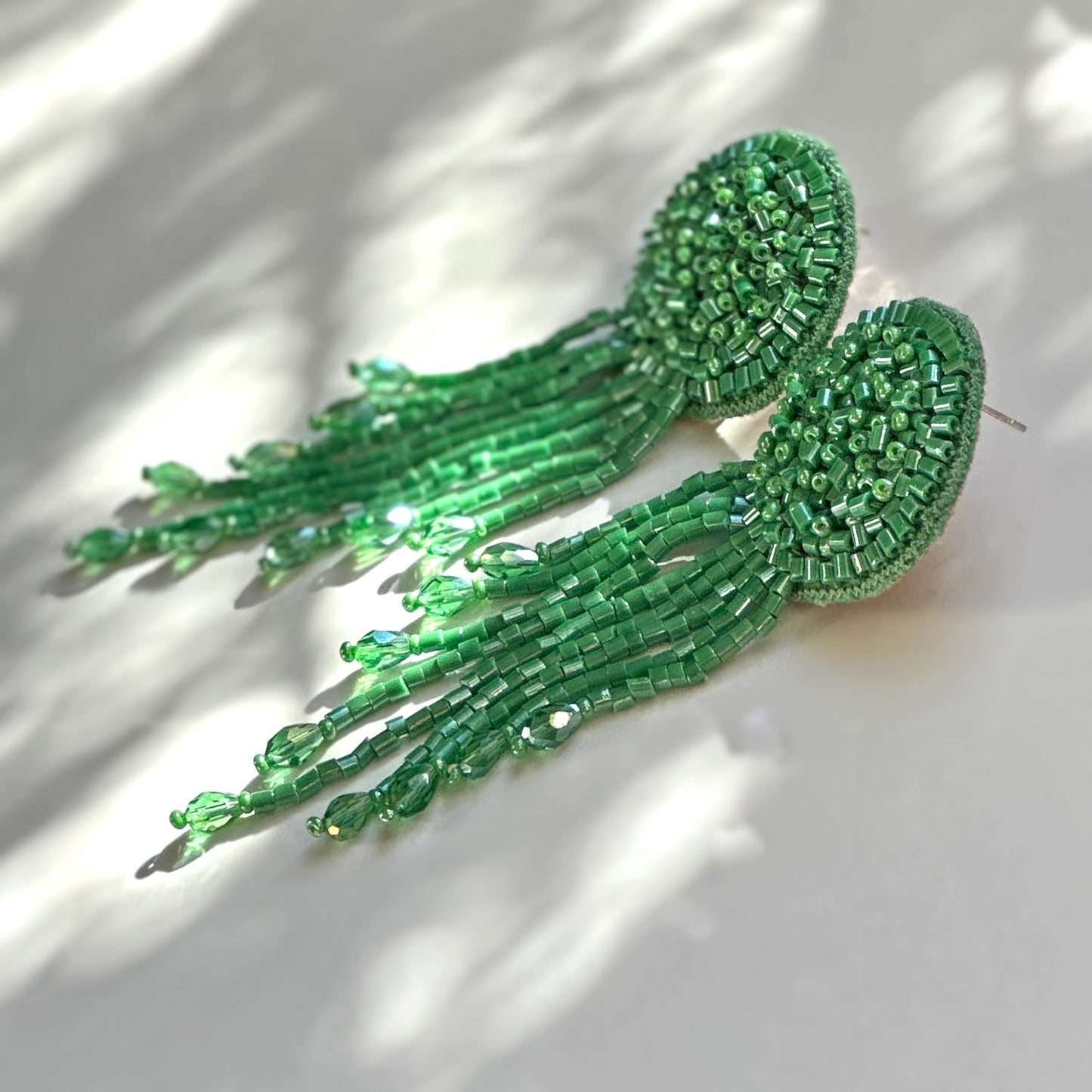 Pair of green glass beaded tassel earrings on shadowy background.