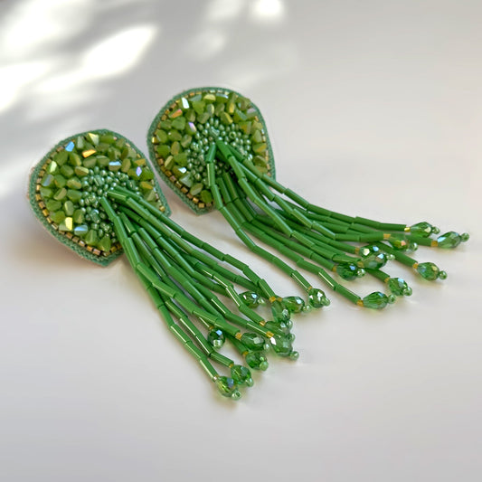Pair of beaded green glass tassel earrings on shadowy background.