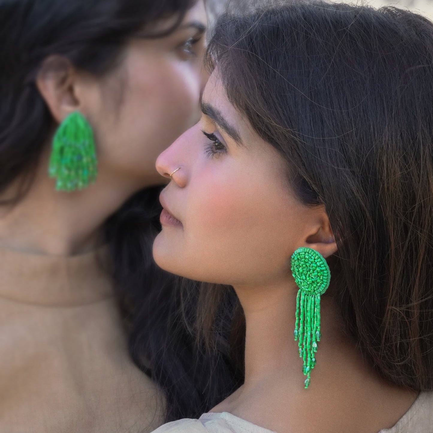 Side image of two women looking in opposite directions, wearing pair of green glass beaded tassel earrings.