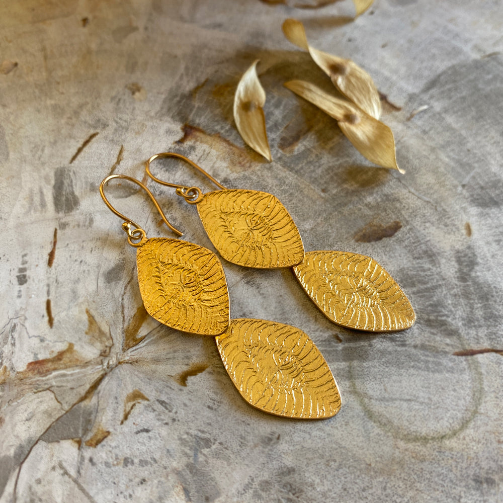 Pair of diamond shaped gold earrings on mottled background.