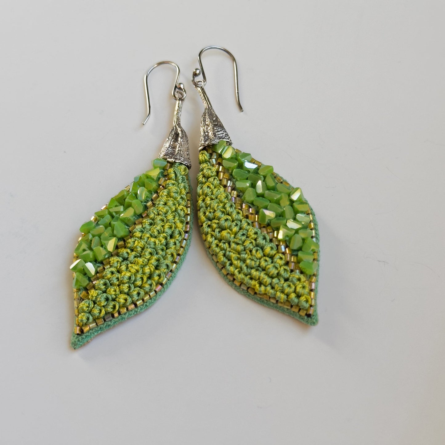 Pair of leaf shaped green glass bead earrings with silver findings on grey background.