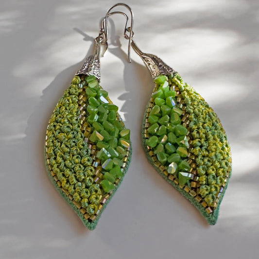 Pair of leaf shaped green glass bead earrings with silver findings on grey and white background.