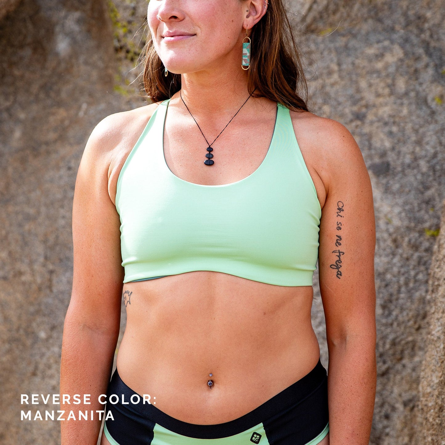 Front view of woman standing in front of rock, wearing light green toura hi- cut sports bra.