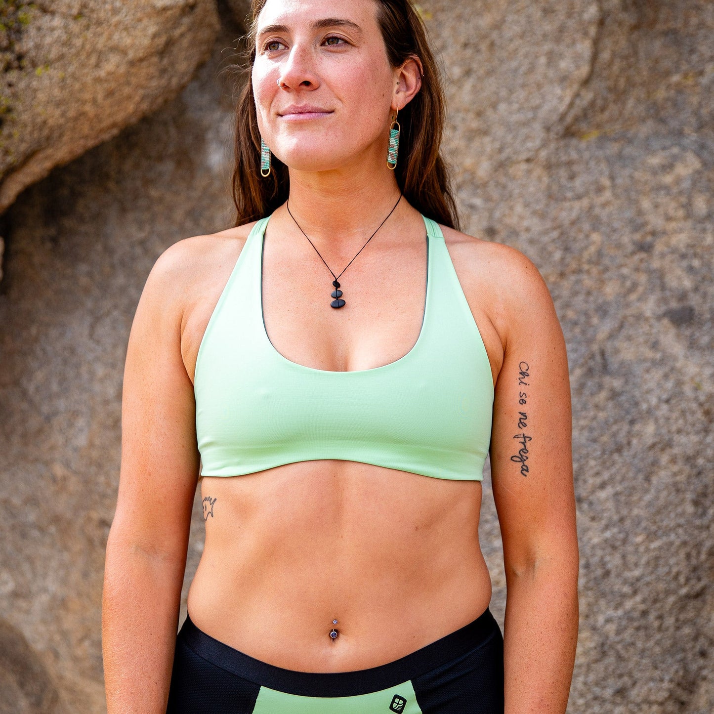 Front view of woman standing in front of rock, wearing light green toura low cut sports bra.