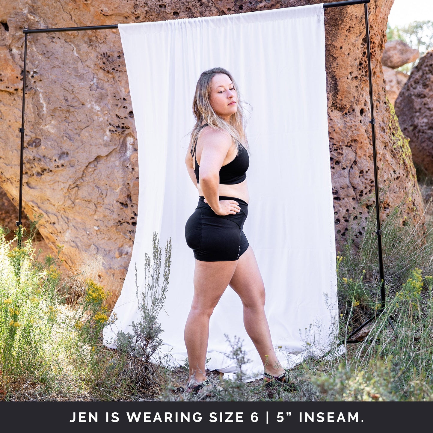 Side view of woman in front of a white sheet, wearing black toura short with 5" inseam.