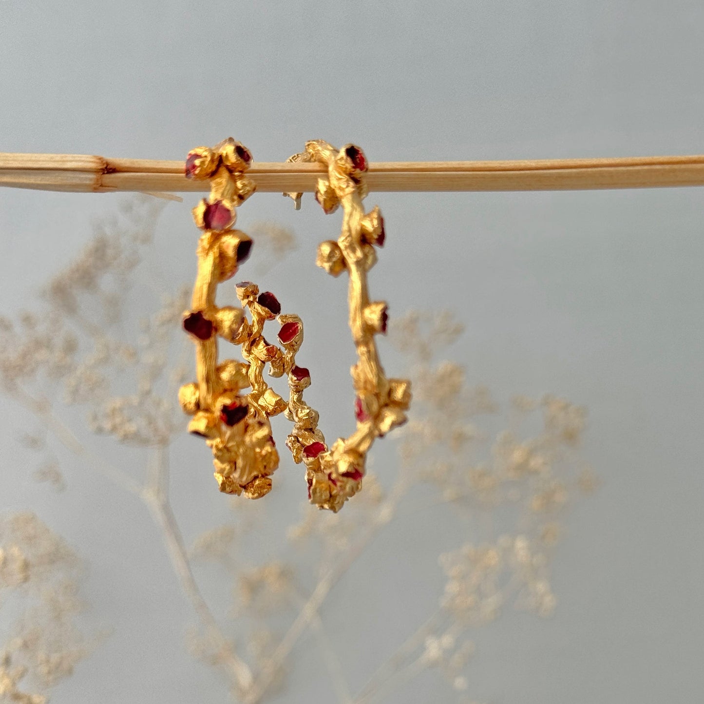 Pair of red and gold hoop earrings hanging on branch.