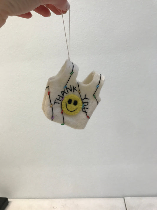 Felt ornament of a white thank you bag with yellow smiley face being held from the string by a hand.