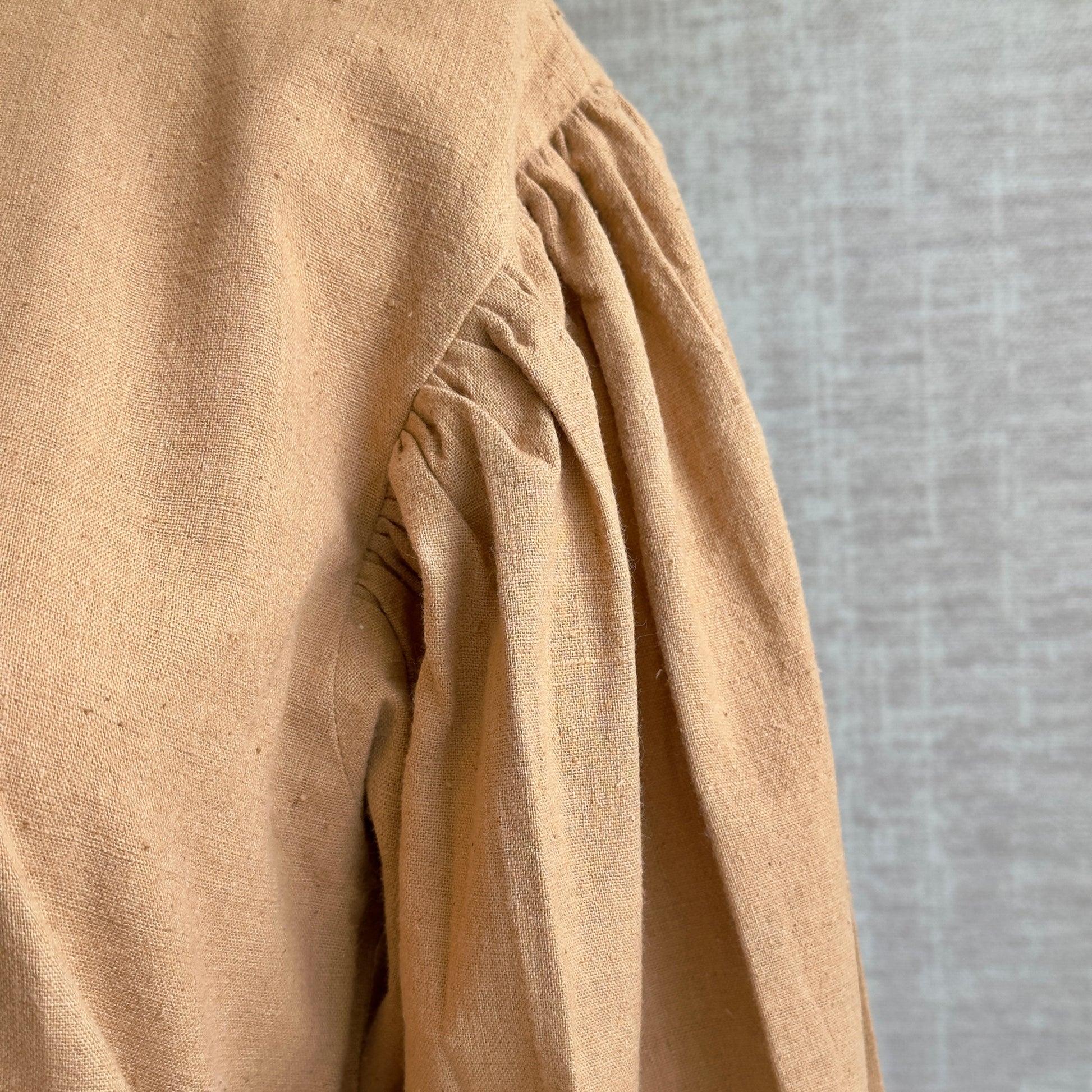 Closeup of sleeve of brown woven long sleeve shirt.
