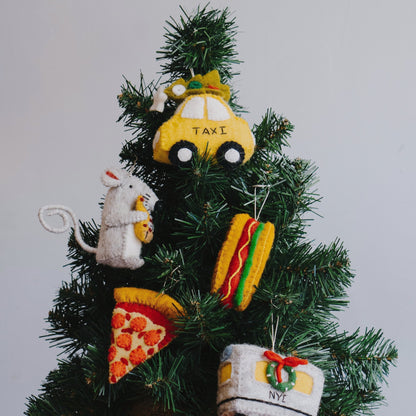Felt ornament of a slice of pepperoni pizza on a Christmas tree with other New York themes ornaments like a taxi, rat, hoagie sandwich, and subway car.