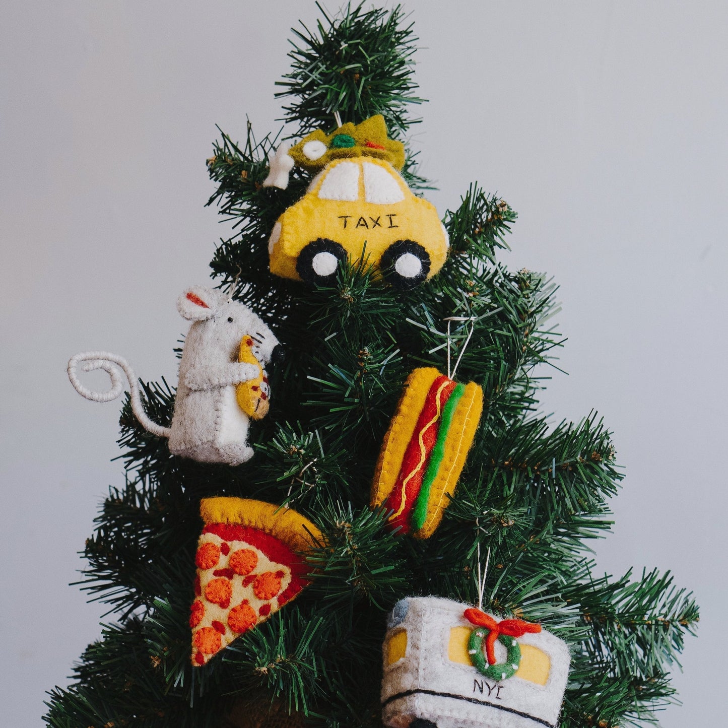 Felt ornament of a New York hot dog with mustard and relish on a Christmas tree with other New York themed ornaments.