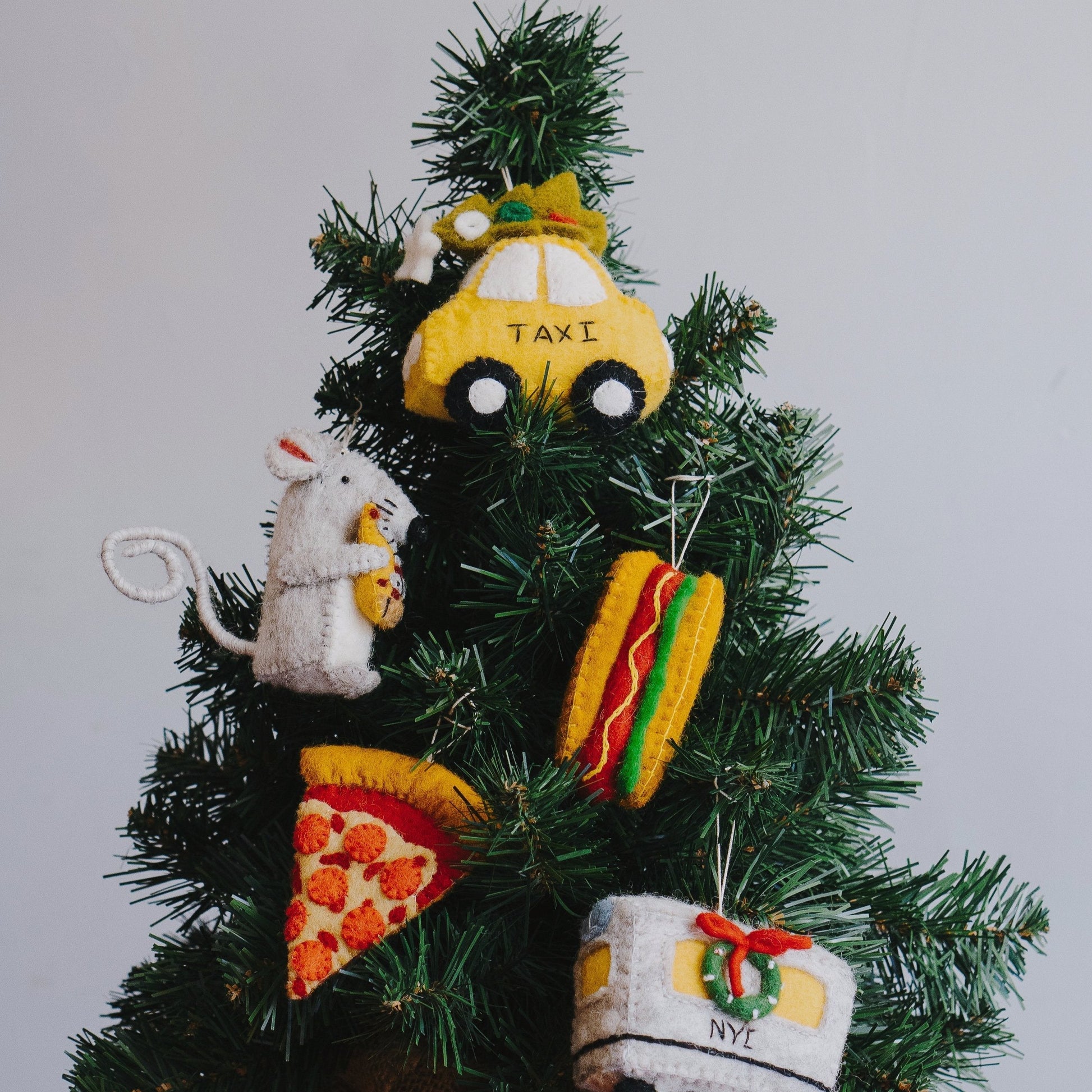 Felt ornament of a New York hot dog with mustard and relish on a Christmas tree with other New York themed ornaments.