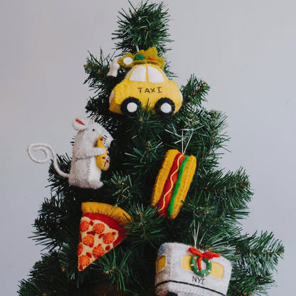 Felt ornament of a New York hot dog with mustard and relish on a Christmas tree with other New York themed ornaments.