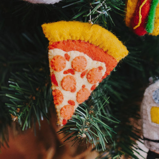 Felt ornament of a slice of pepperoni pizza hanging on a Christmas tree.