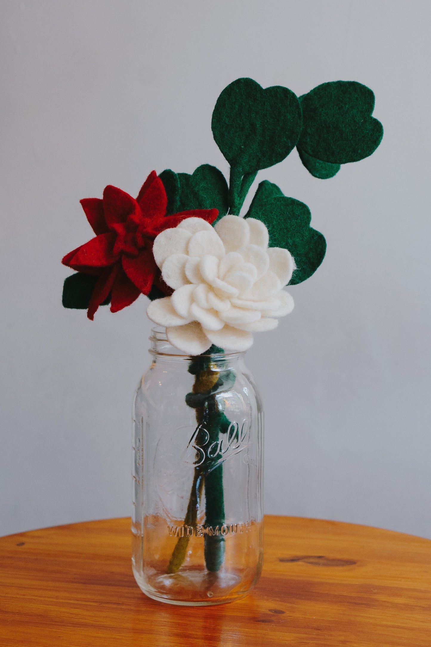 Red and white felt Poinsettia flowers in a glass vase with other felt greenery.