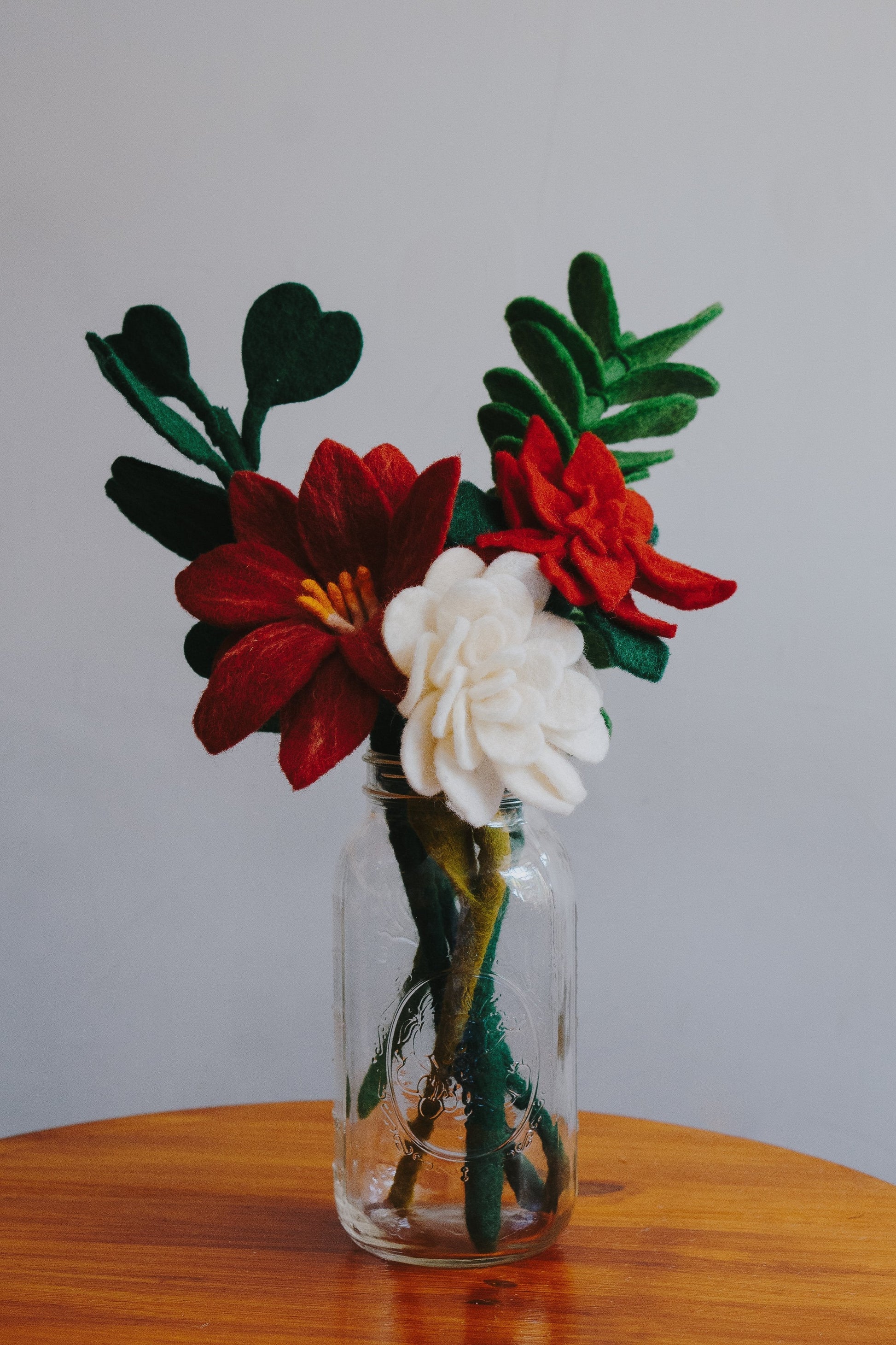 Red and white felt Poinsettia flowers in a glass vase with other felt greenery.
