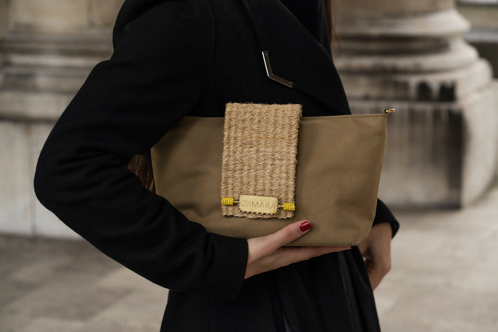 Partial view of woman in black holding sandstone green bag under her arm.