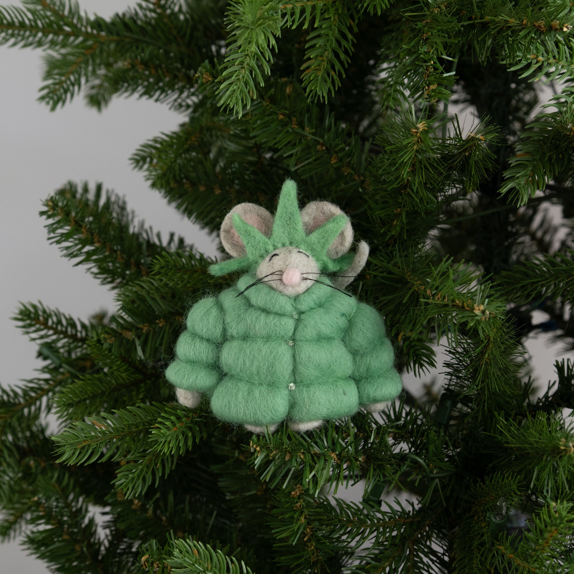 Felt ornament of a mouse in a green puffer jacket and statue of liberty crown on a Christmas tree.