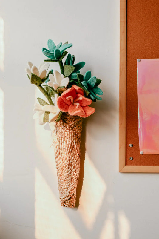 Brown woven wall vase with felt flowers, hanging on wall.