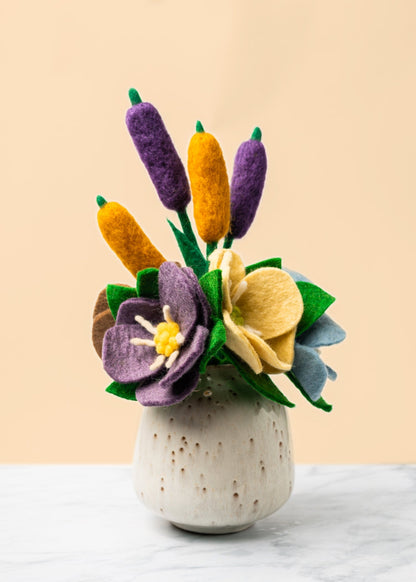 Purple, yellow, and blue felt Hepatica flowers in a tan round vase with felt Cattails.