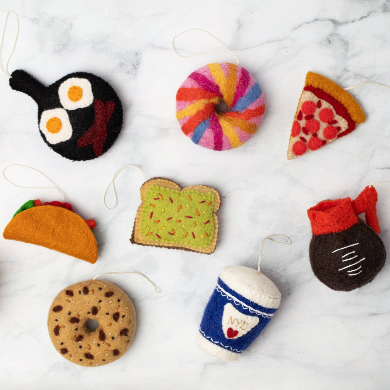 Felt ornament of a coffee cup with a blue sleeve that has NYC and a red heart on it scattered with other various food ornaments.