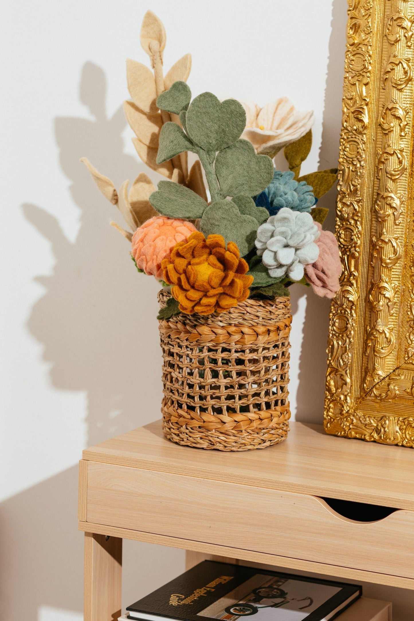Various felt Geranium flowers in brown woven vase with felt leaves.