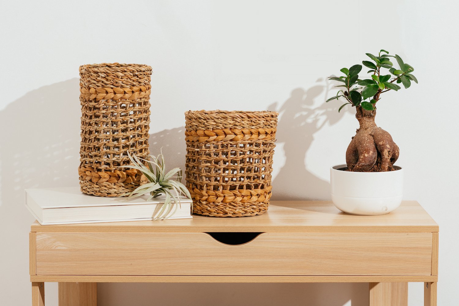 Short and tall brown woven vase with glass inserts on brown table.